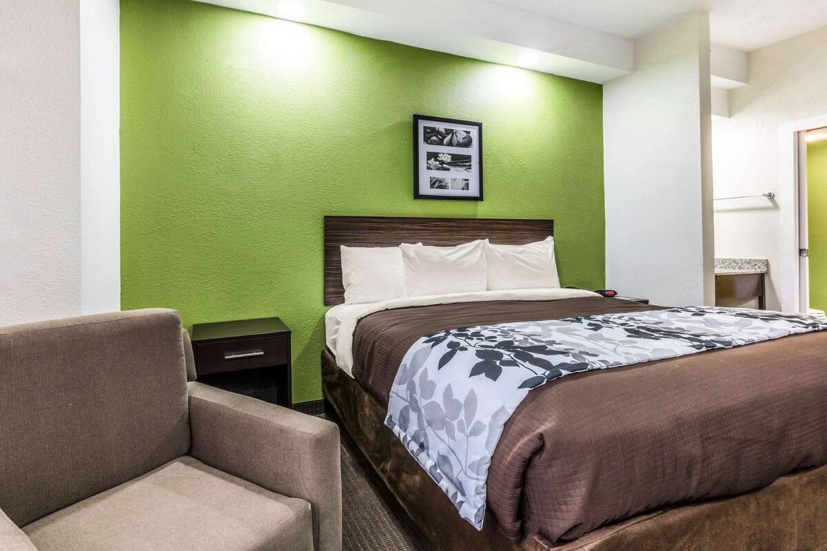 A hotel room with a bed, a chair, a nightstand, and a green wall.