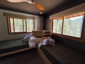 Ein Zimmer mit zwei Etagenbetten, einem Deckenventilator und Fenstern mit Blick auf einen Wald.