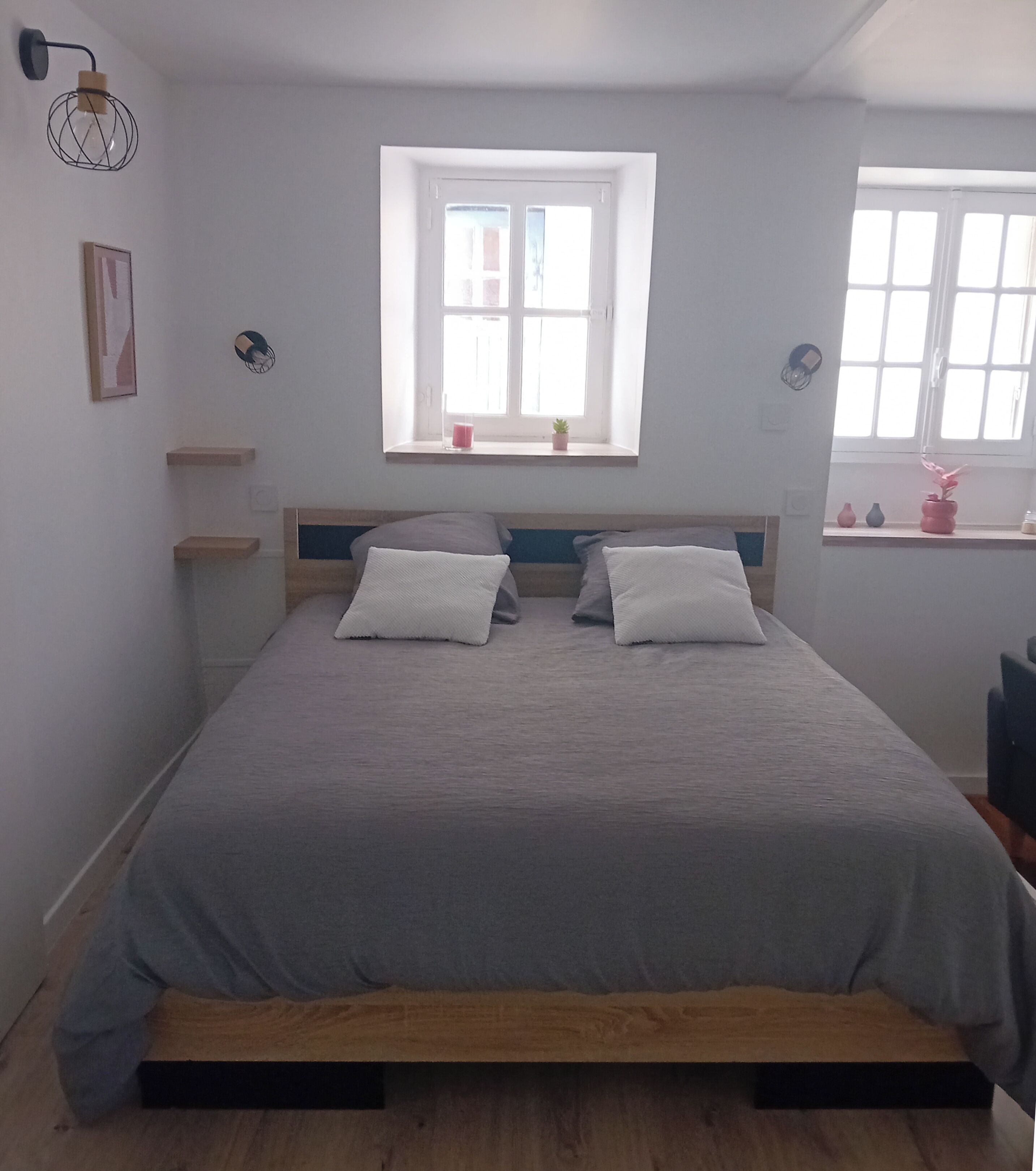 A bedroom with a bed, a window, and a small shelf with a plant.