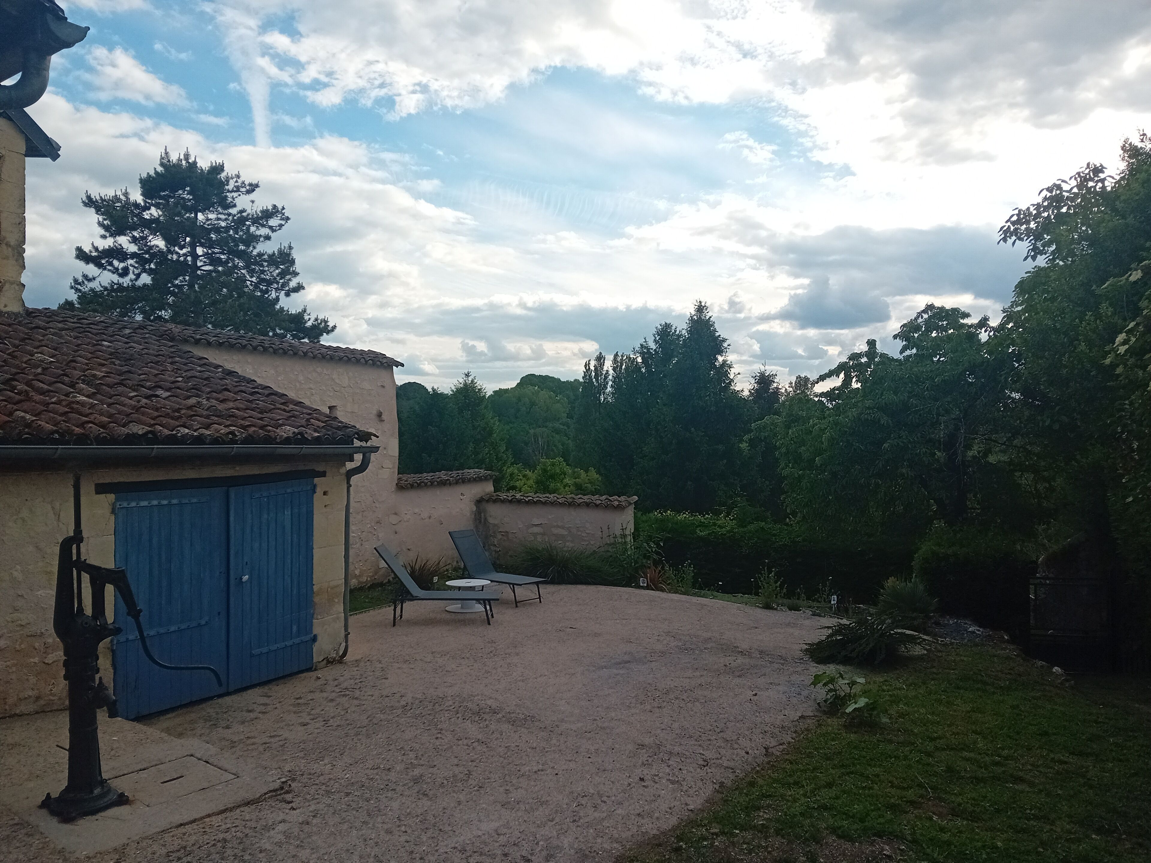 A building with a blue door, a water pump, and a gravel patio with two lounge chairs.
