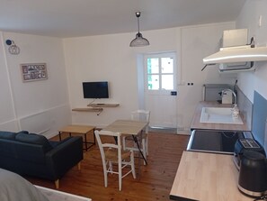 Ein kompakter Wohnbereich mit Sofa, Esstisch, Stühlen, Fernseher, Küchenzeile und einer zur Außenseite führenden Tür.
