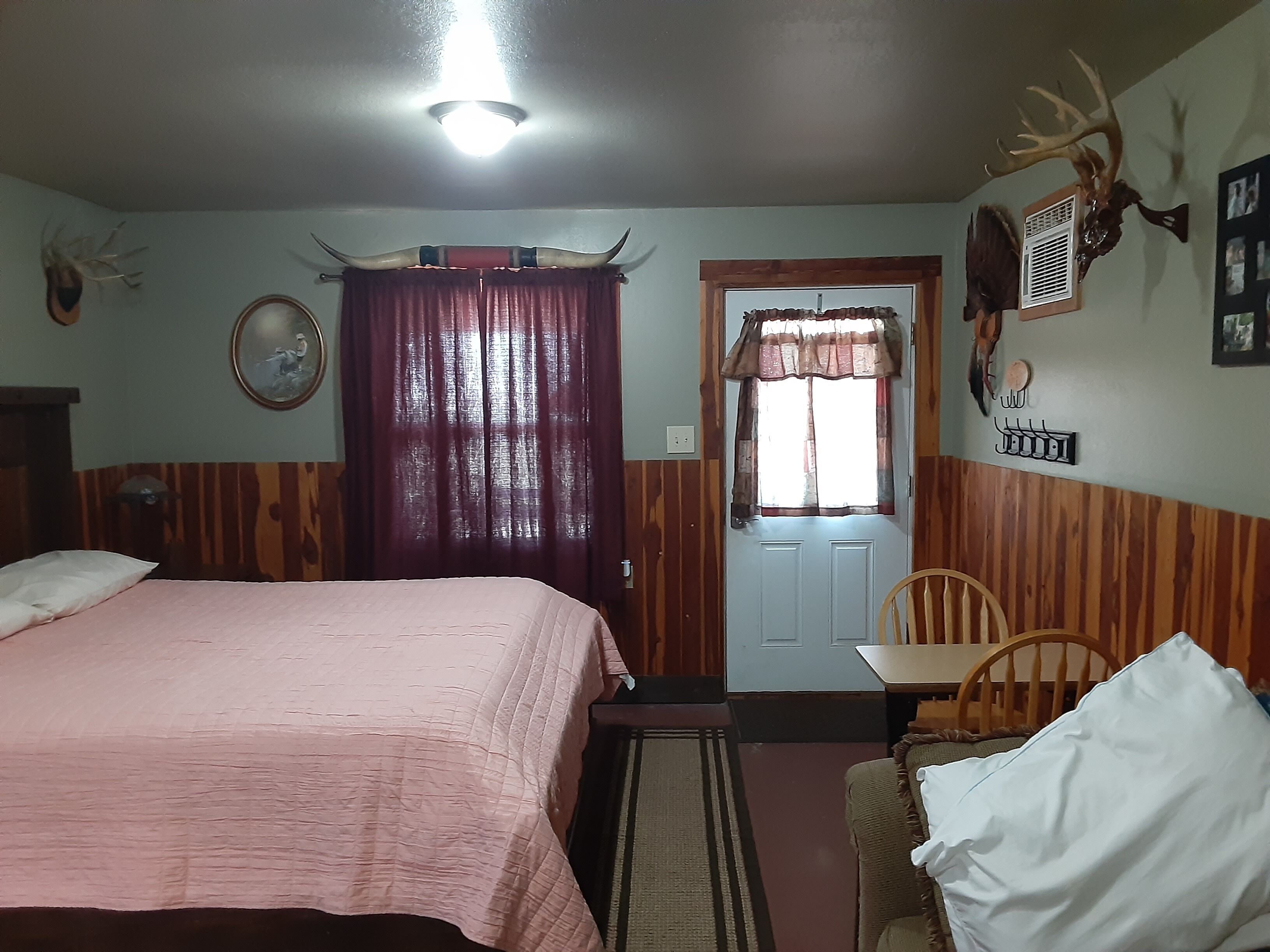 Un dormitorio con cama, una silla, una puerta y un ventilador fijado a la pared.