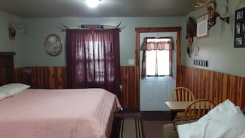 Un dormitorio con cama, una silla, una puerta y un ventilador fijado a la pared.