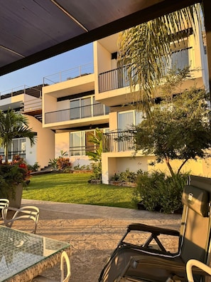 Un edificio moderno con numerosi balconi, area salotto esterna e un'ampia vegetazione.