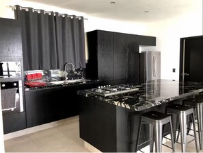Een moderne keuken met zwarte kasten, een marmeren eiland, roestvrijstalen apparatuur en een bar met krukken.