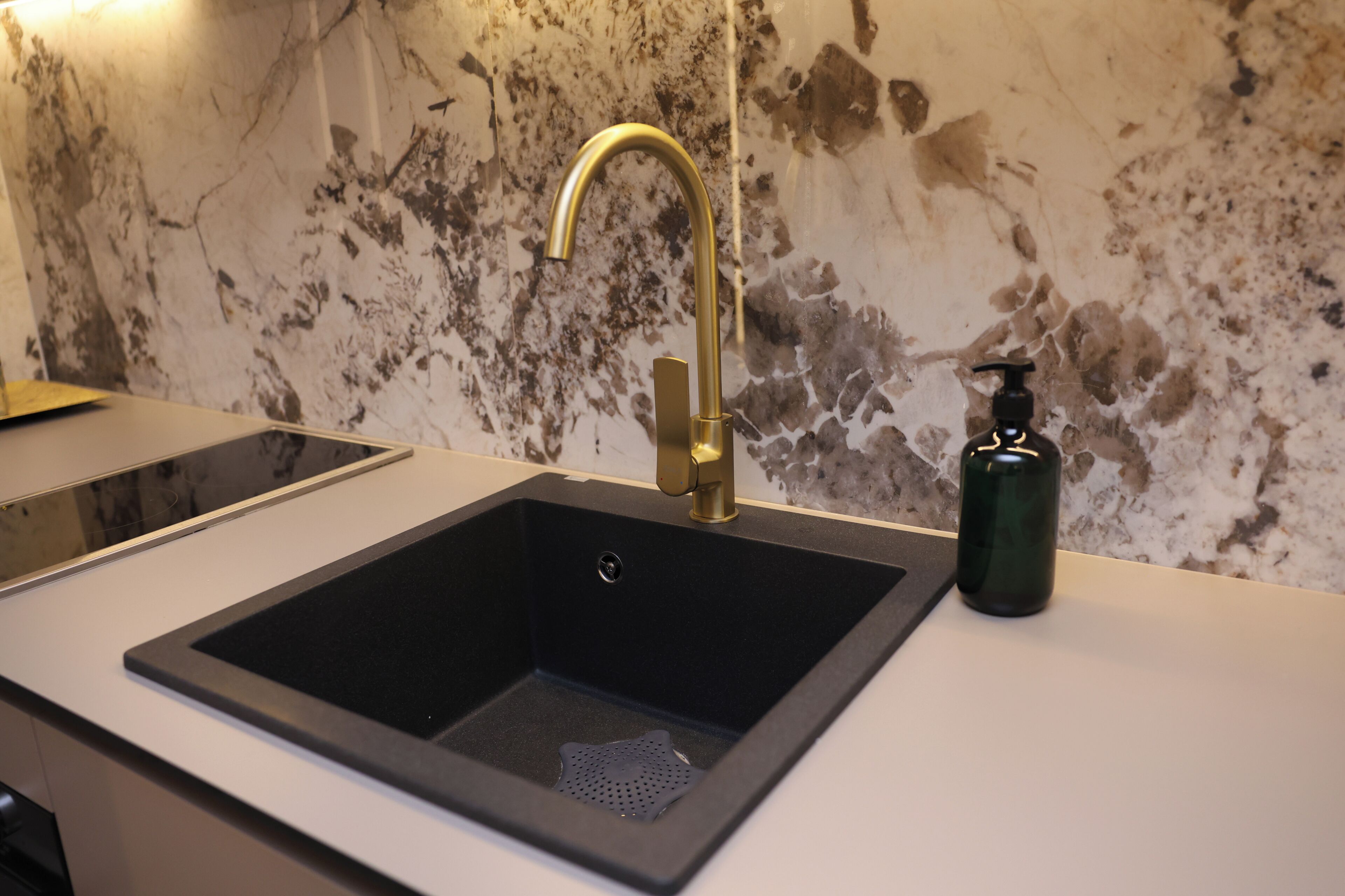 A bathroom sink with a gold faucet, a soap dispenser, and a marble-patterned wall.