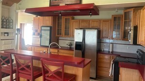 Una cocina con armarios de madera, un refrigerador de acero inoxidable, una barra roja y un cuadro con botellas de vino.