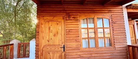 A wooden cabin with a large door and a window, a balcony, and a table.