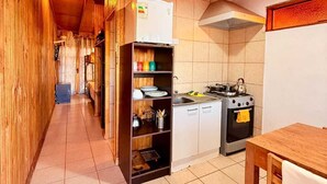 A narrow kitchen with wooden walls, a tiled floor, a refrigerator, a stove, and a wooden table.