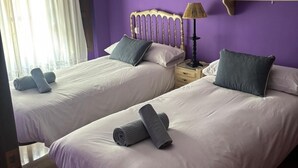 A room with two beds, a hanging light fixture, a wall-mounted shelf, and a window with curtains. - Paquita's House (Priego de Córdoba)