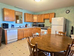 A kitchen with wooden cabinets, a white refrigerator, a microwave, a dishwasher, and a dining table with chairs.