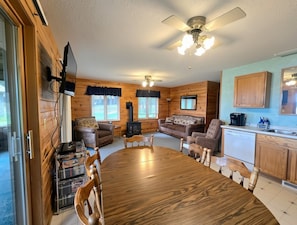 A cozy cabin interior with a dining table, sofas, a kitchen area, and a ceiling fan. - Willow at Evergreen Bay Resort on Boot Lake (Park Rapids)