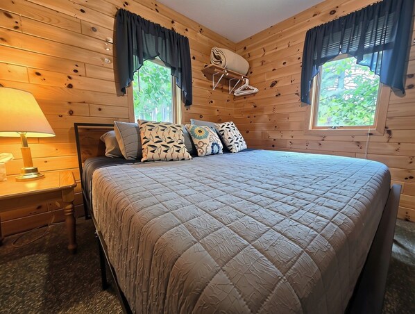 A wooden-paneled room with a bed, a desk, and a lamp.