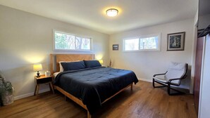 Una camera da letto con un letto in legno, abat-jour, una sedia e due finestre.