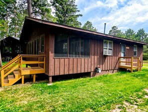 A wooden cabin with a porch and a staircase leading to the entrance. - Tamarack at Evergreen Bay Resort on Boot Lake (Park Rapids)