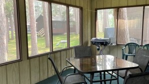 Une pièce avec une table en verre et des chaises en métal, de grandes fenêtres et un ventilateur de plafond.