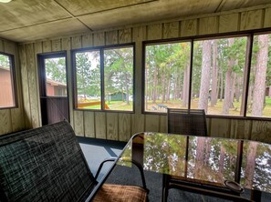A room with a wooden paneled wall, a window with a view of trees, a table, and a bench.