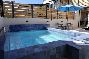 A rectangular hot tub with a tiled edge, a wooden fence, and a blue umbrella. - Isla Verde Ocean Breeze | Luxury Beach Suites 2E (Carolina)