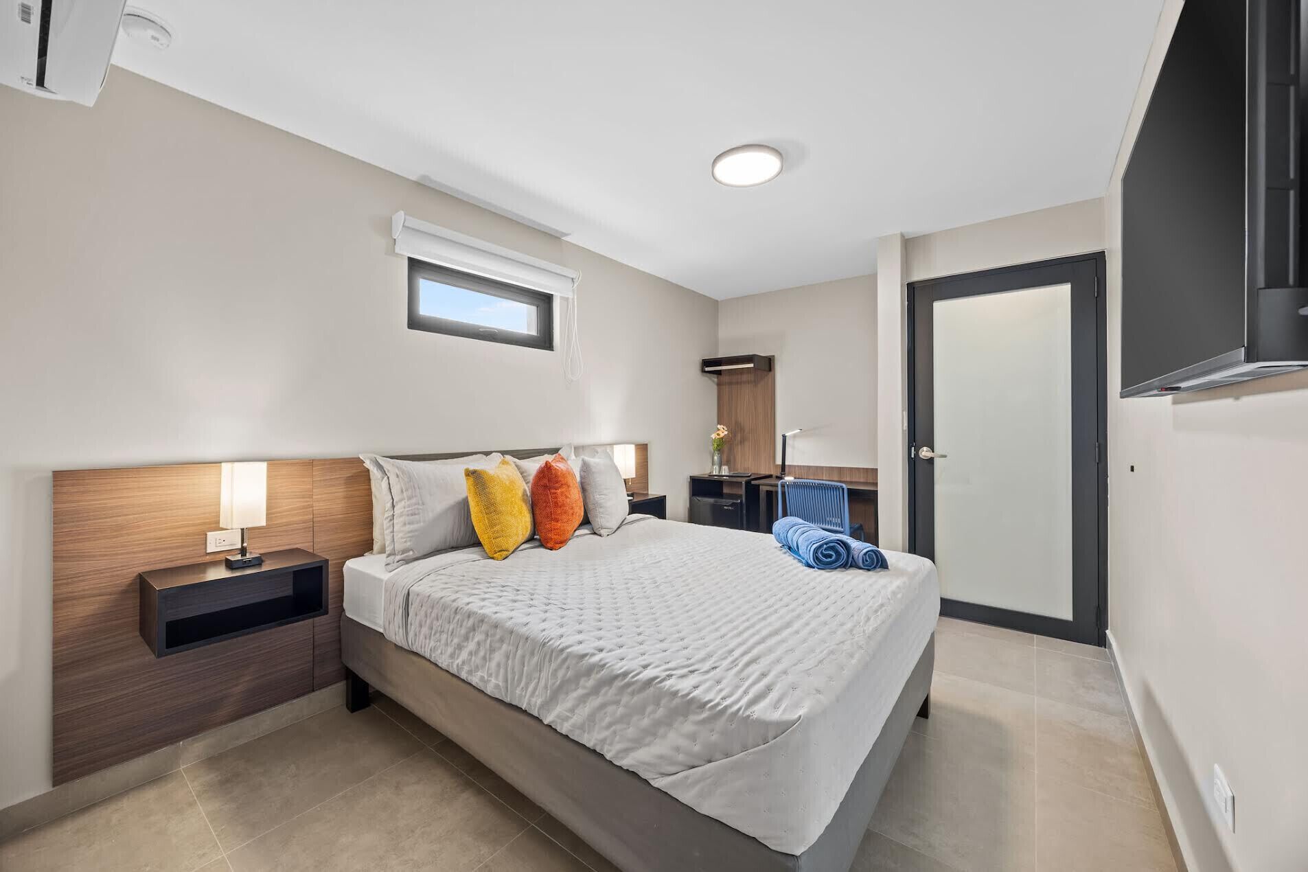 A modern hotel room with a large bed, bedside tables, a desk, and a wardrobe.