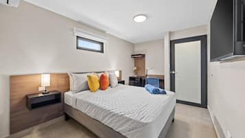 A modern hotel room with a large bed, bedside tables, a desk, and a wardrobe.