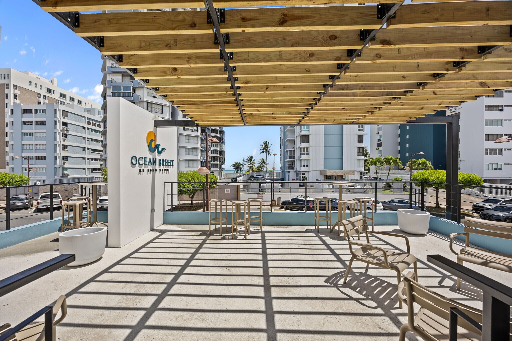 A rooftop terrace with outdoor seating, a sign for Ocean Breeze at Asia Term, and modern buildings in the background.
