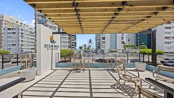 A rooftop terrace with outdoor seating, a sign for Ocean Breeze at Asia Term, and modern buildings in the background.