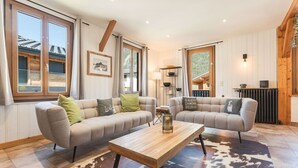 Ett rymligt vardagsrum med två soffor, ett soffbord och ett stort fönster med utsikt över omgivningen.