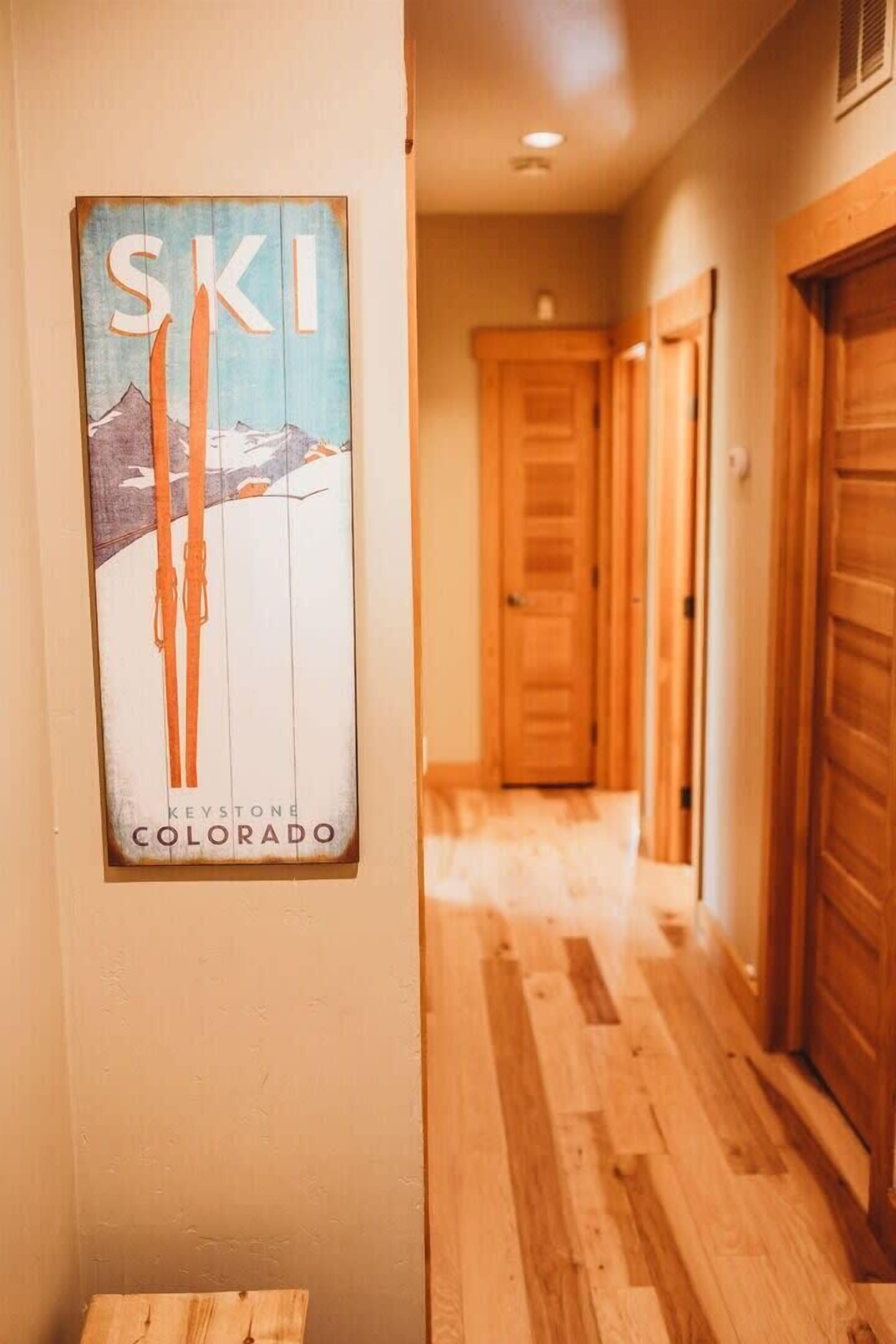 Ein Flur mit Holzboden, einer Holztür und einem an der Wand befestigten Schild mit den Aufschriften 'SKI' und 'KEYSTONE COLORADO'.