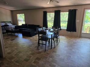 A spacious living area with a dining table, black sofa, and a ceiling fan.