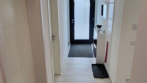 Un pasillo con una puerta al final, un lavamanos pequeño y un espejo en la pared.