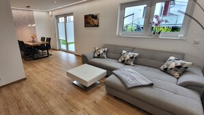 Una sala de estar moderna con un sofá gris, una mesa de centro blanca y un comedor con mesa y sillas.