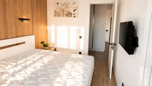 Quarto moderno com cama grande, guarda-roupa de madeira e televisão de ecrã plano na parede.
