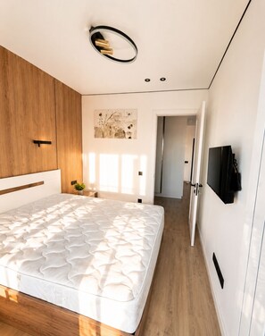 Ein modernes Schlafzimmer mit einem großen Bett, einem Holzschrank und einem flachbildfernseher an der Wand.