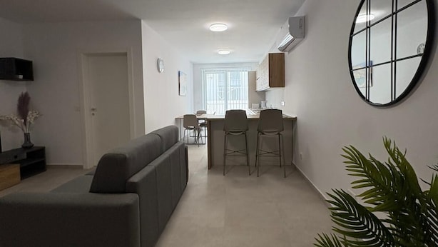 Una sala de estar moderna con un sofá, un comedor con mesa y sillas, y una cocina con un equipo de aire acondicionado.