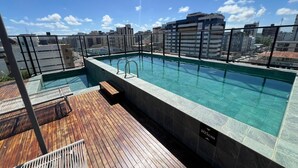En pool på taget med klart vand, omgivet af en træterrasse og udsigt over bybilledet.