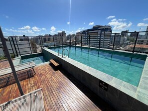 Ein Pool auf dem Dach mit klarem Wasser, umgeben von einer Holzterrasse und Blick auf die Stadt.