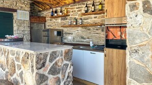 Une cuisine aux murs en pierre, avec un plafond en bois, des appareils électroménagers intégrés et un meuble à vin.