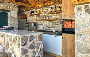 Eine Steinküche mit Holzbalkendecke, eingebauten Geräten und einem Weinkühlschrank.