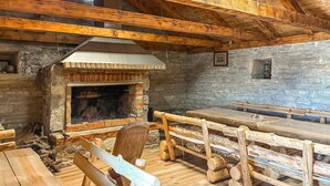 Une cheminée en pierre rustique avec une hotte, des bancs en bois et un mur en pierre.