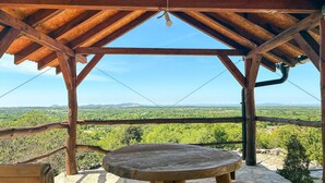 Un belvédère en bois, avec une table et un banc, offrant une vue sur un paysage verdoyant.