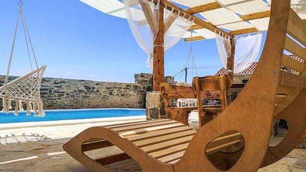 Une terrasse en bois avec une piscine, un mur en pierre et un fauteuil suspendu.