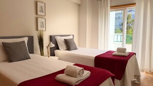 A hotel room with two beds, a window with curtains, and a view of greenery outside. - Old Town Albufeira Retreat (Albufeira)