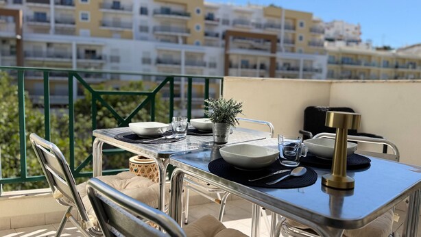 A balcony with a table set for dining, chairs, a small potted plant, and a water pitcher. - Old Town Albufeira Retreat (Albufeira)