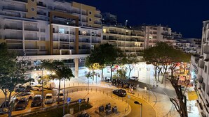 A multi-story building with balconies, a parking area, and a pedestrian zone with trees and shops. - Old Town Albufeira Retreat (Albufeira)