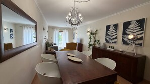 A dining area with a wooden table, white chairs, a chandelier, and fern artwork on the walls. - Old Town Albufeira Retreat (Albufeira)