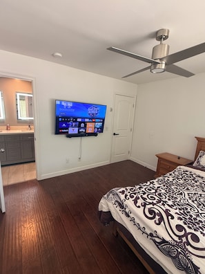Ein Schlafzimmer mit einem Bett, einem Deckenventilator, einem an der Wand montierten Fernseher und einem Holzboden.