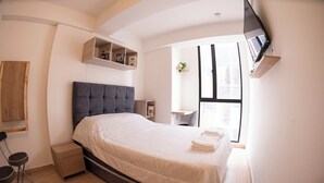 A bedroom with a bed, a desk, a chair, a TV, and a window. - Corazón fotográfico  (Bogotá)