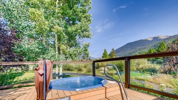 Un bain à remous sur une terrasse en bois, avec vue sur une forêt et des montagnes.