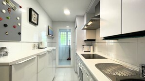 A narrow kitchen with white cabinets, a stainless steel sink, and a microwave. - Modern 2-bedroom Apartment With Private Underground Parking Lift Access (Marbella)