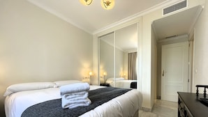 A hotel room with a bed, a dresser, a mirror, and a door. - Modern 2-bedroom Apartment With Private Underground Parking Lift Access (Marbella)